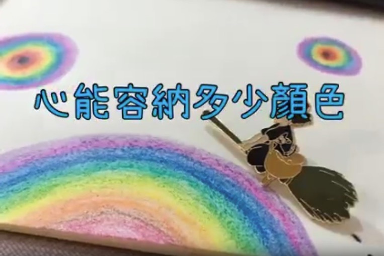 一張以「心能容納多少顏色」為主題的手繪圖，畫面中有彩虹漸層色彩的圖畫，以及一個《魔女宅急便》琪琪騎著掃帚的金色胸針。